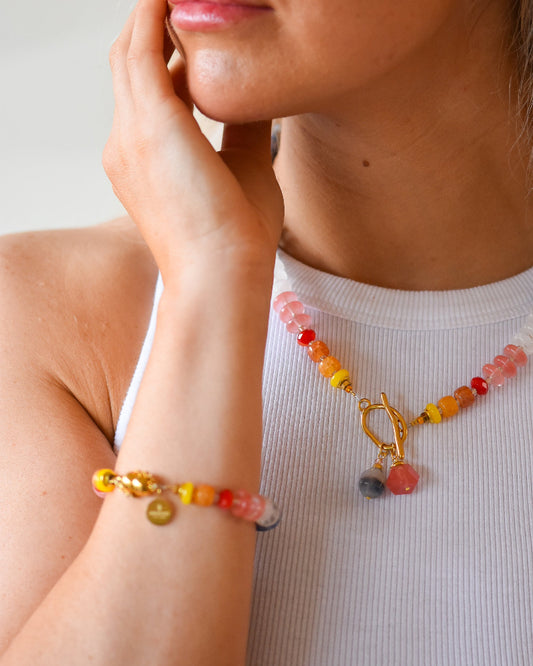Close-up of a person wearing a colorful beaded bracelet and necklace with a neutral background
