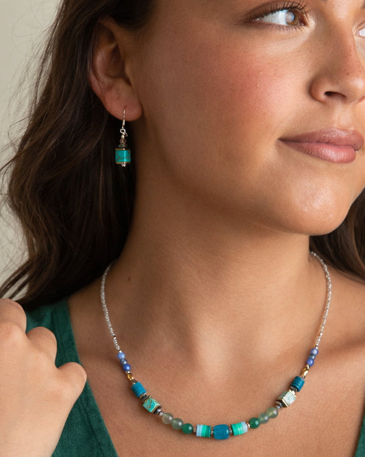 Woman wearing a green top with a necklace and earrings, against a neutral background