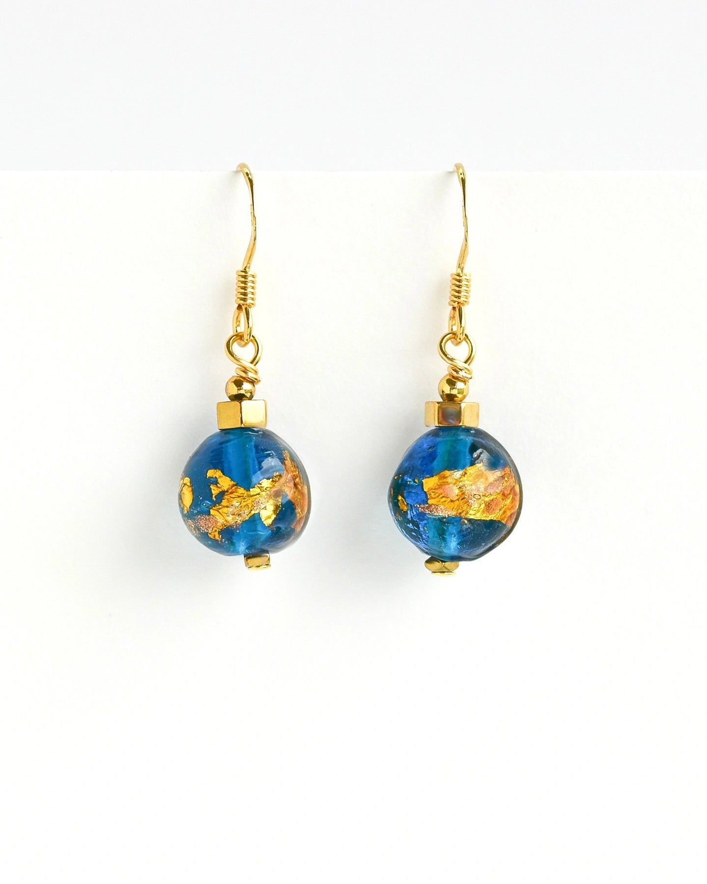 A pair of gold-tone dangle earrings with round blue glass beads containing gold leaf patterns, shown against a plain white background.