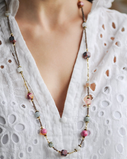 Long gemstone necklace with pink and gey beads on a white blouse