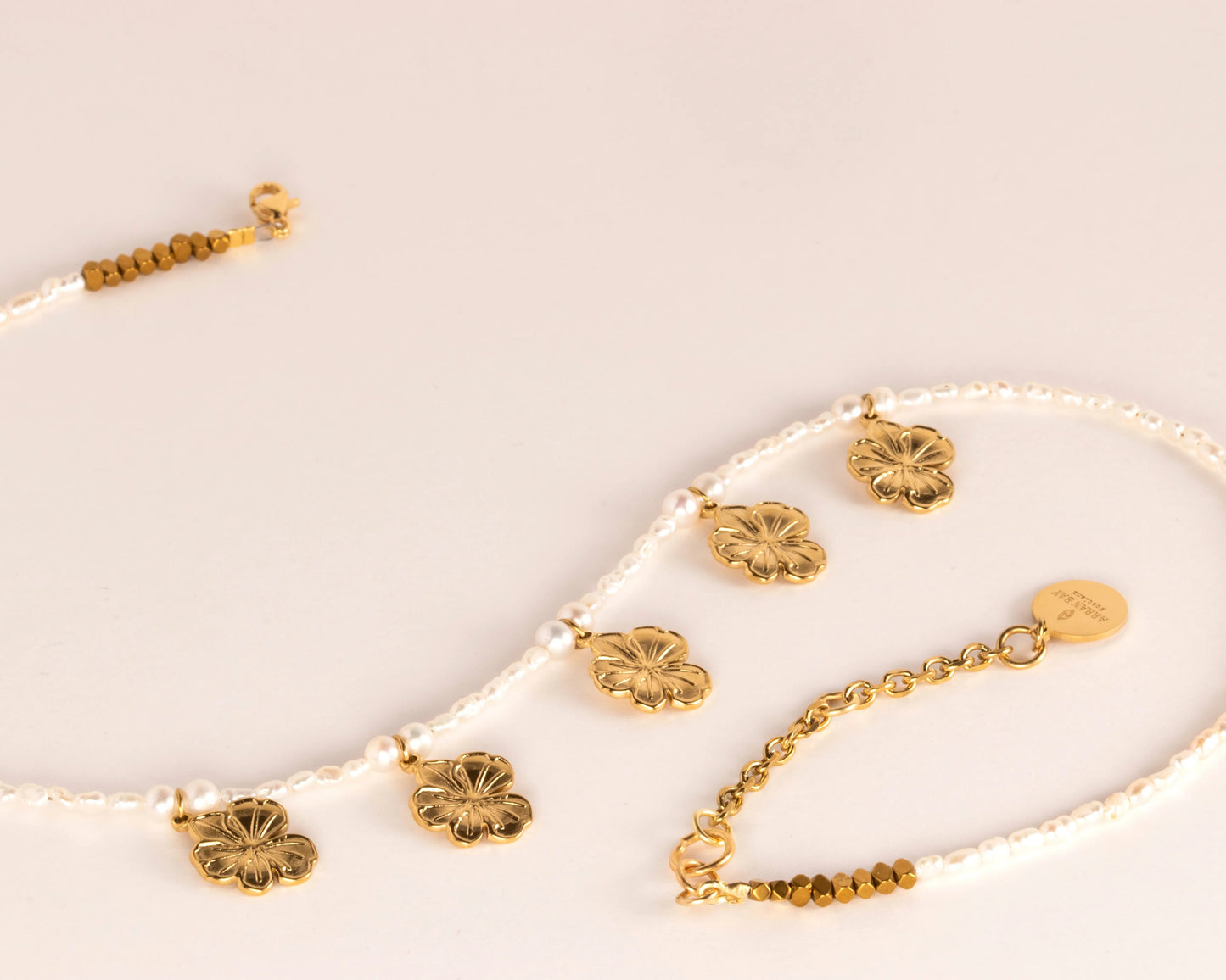 Gold & pearl necklace with floral pendants on a light beige background