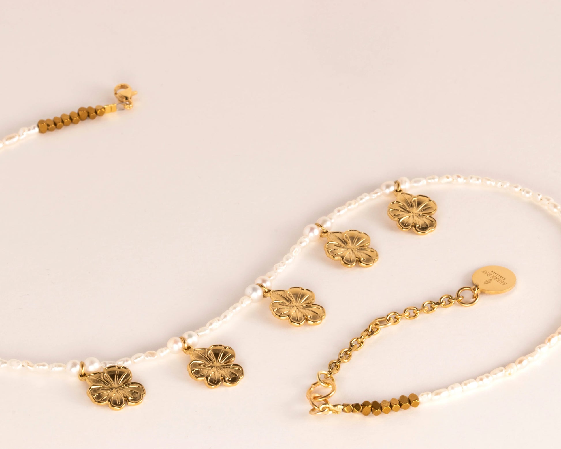 Gold & pearl necklace with floral pendants on a light beige background