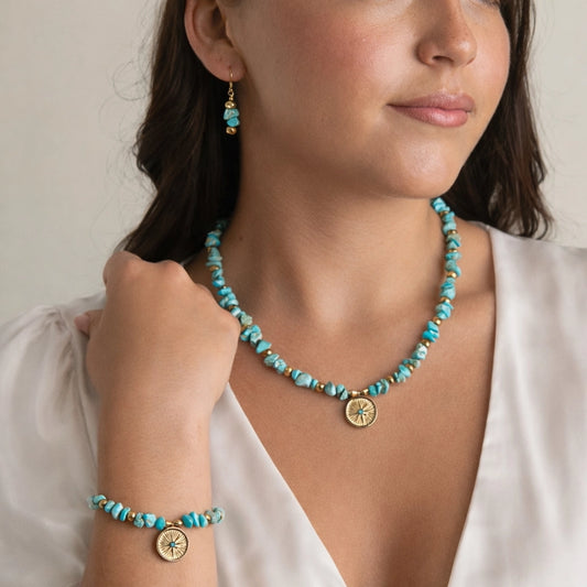 Woman wearing a turquoise necklace and bracelet with gold accents on a neutral background